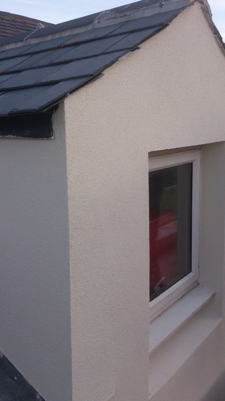 A dormer finished in cream render over external wall insulation, the reveals returned neatly into the window