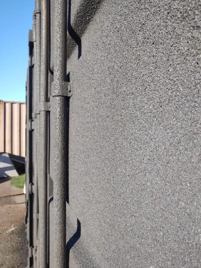 Spray cork over the corrugated steel side of a shipping container, the ribs still reading through