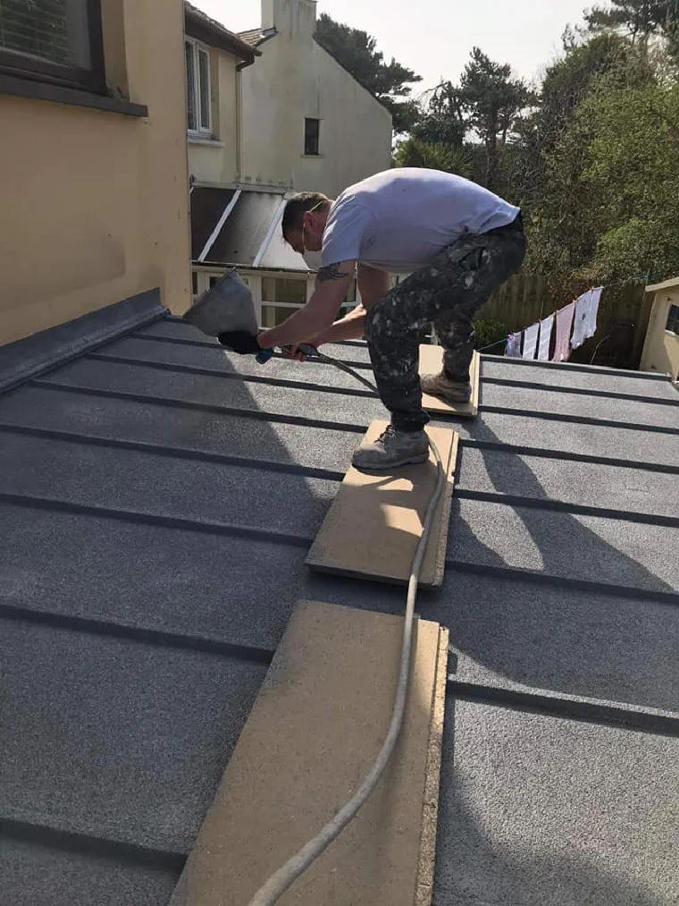 Spraying cork render across a conservatory roof, working off scaffold boards laid over the panels