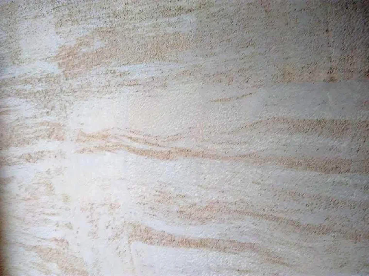A travertine-effect plaster finish with warm banding and an open, pitted texture