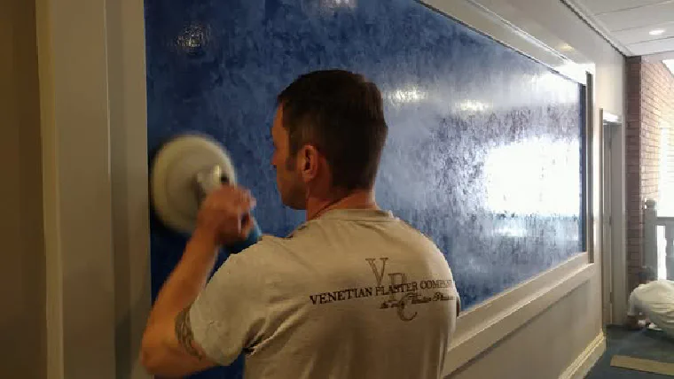 A polishing machine being worked across a deep blue Venetian plaster panel