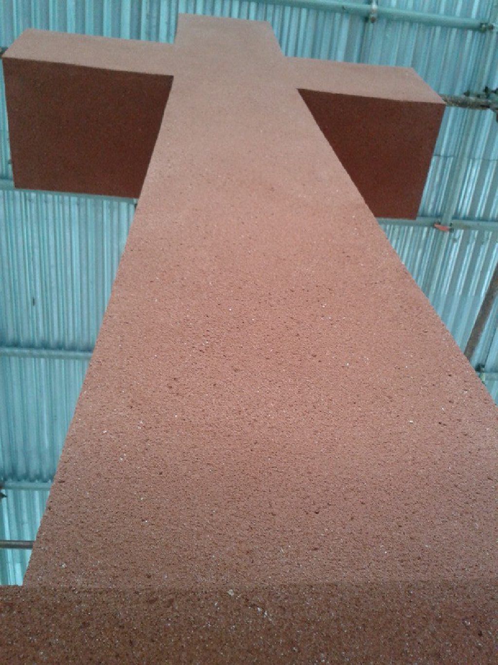 The cross head finished in terracotta render, seen from below under the scaffold roof