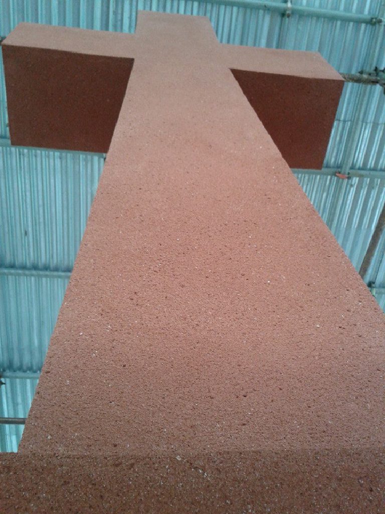 The cross head finished in terracotta render, seen from below under the scaffold roof