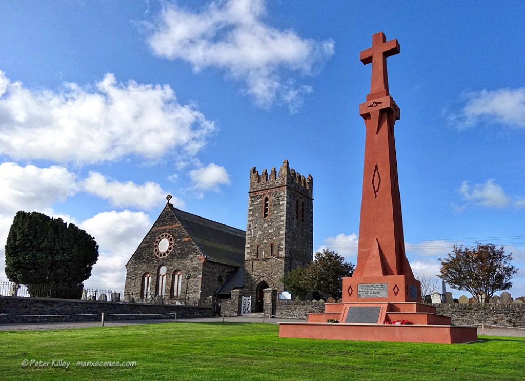 The finished memorial in weathered terracotta render, with Andreas church behind it under a blue sky