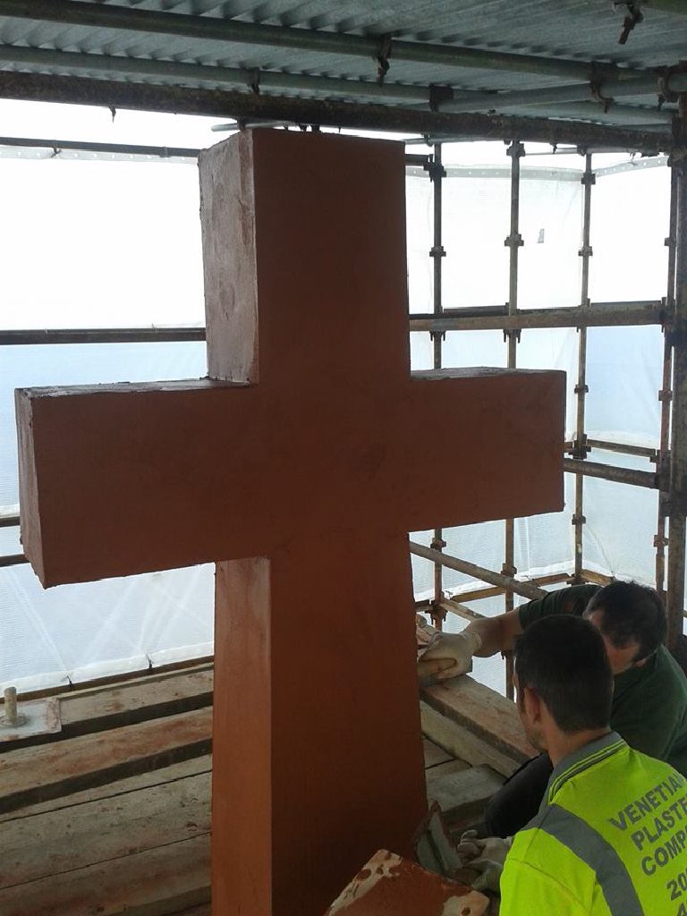 The cross with its first terracotta coat on, two of the team working the arm below