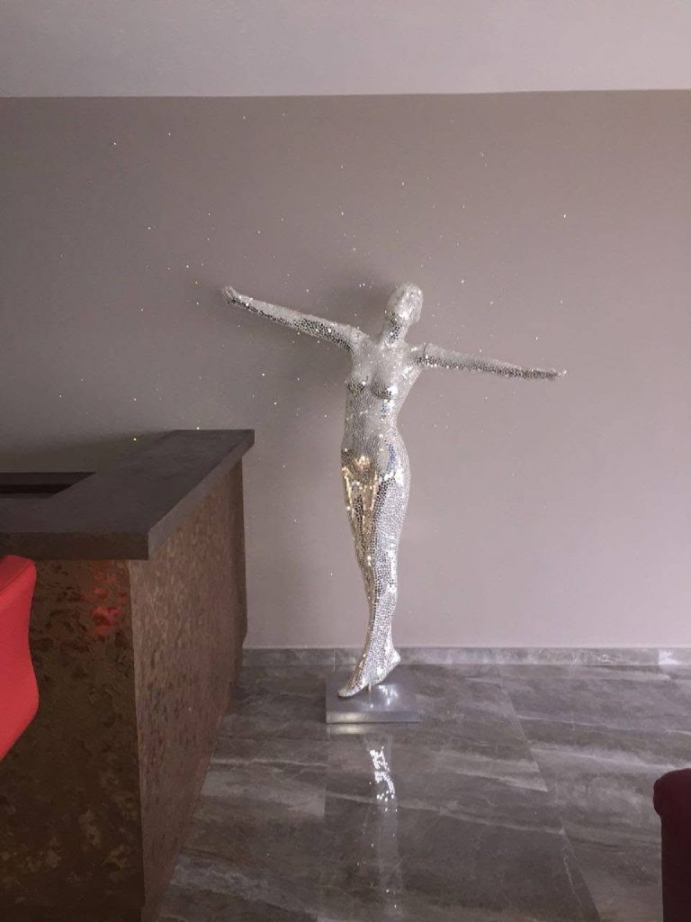 The mirror-mosaic statue catching the bronze reflections beside the bar