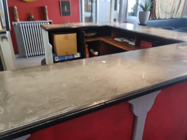The bar top in plain grey microcement, running round the corner of the L with the red wall behind