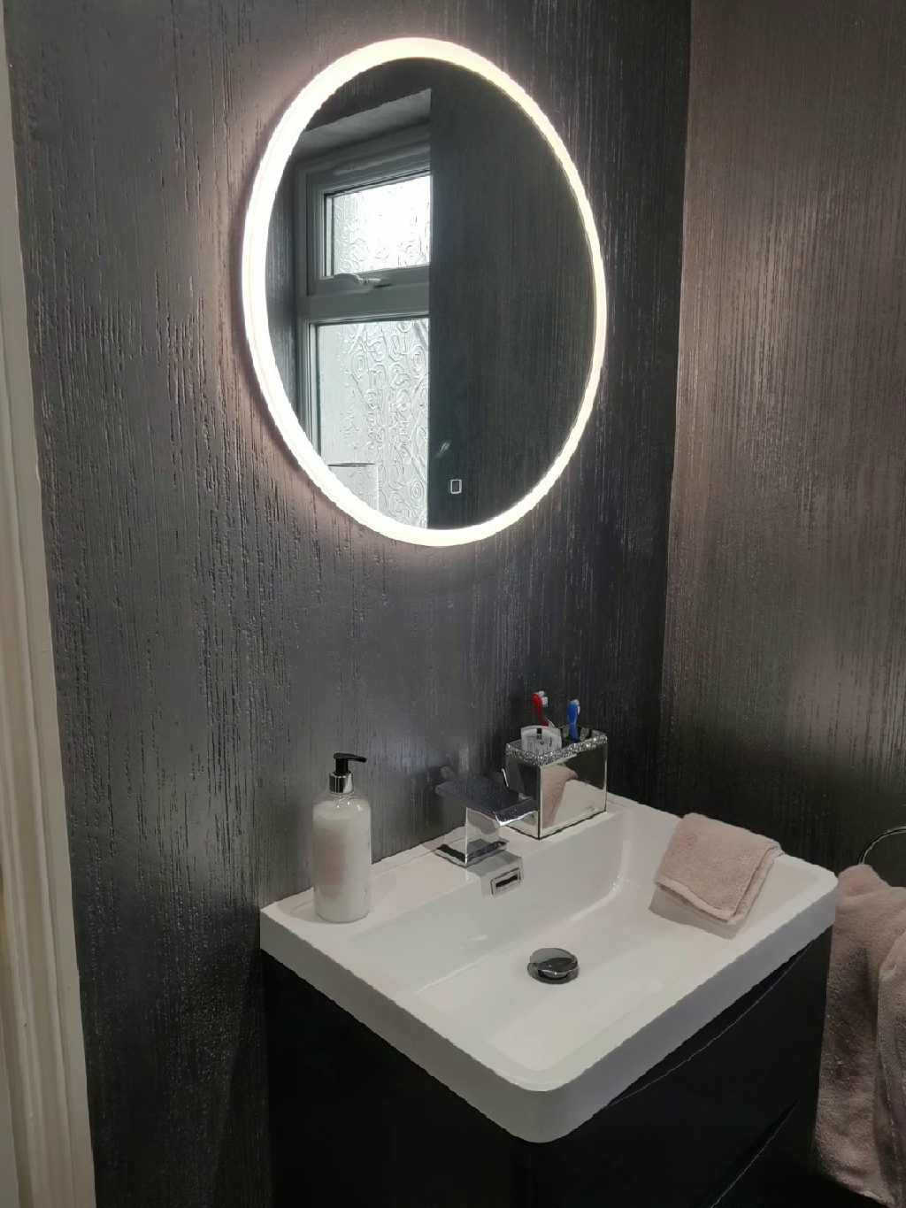 The basin and backlit round mirror against the metallic silver wall