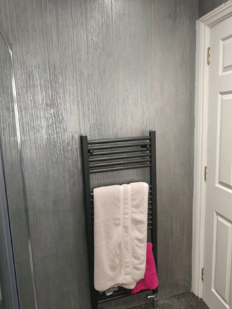 The black towel radiator against the metallic silver plaster, quartz floor below