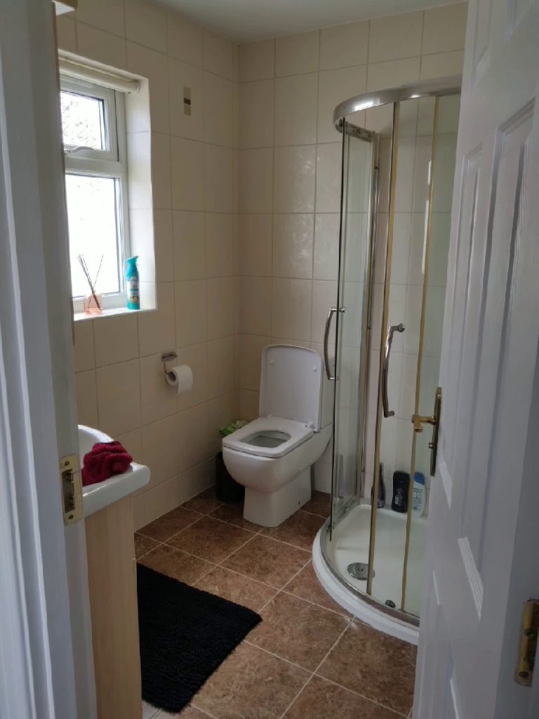 The bathroom before the work, cream wall tiles, brown floor tiles and a corner shower