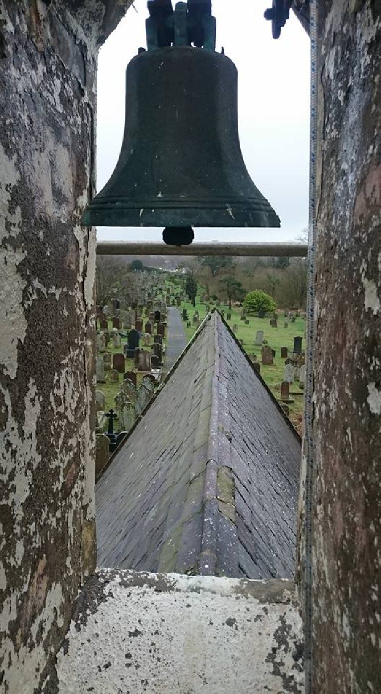 The bell seen through the tower opening, slate roof ridge and the cemetery beyond