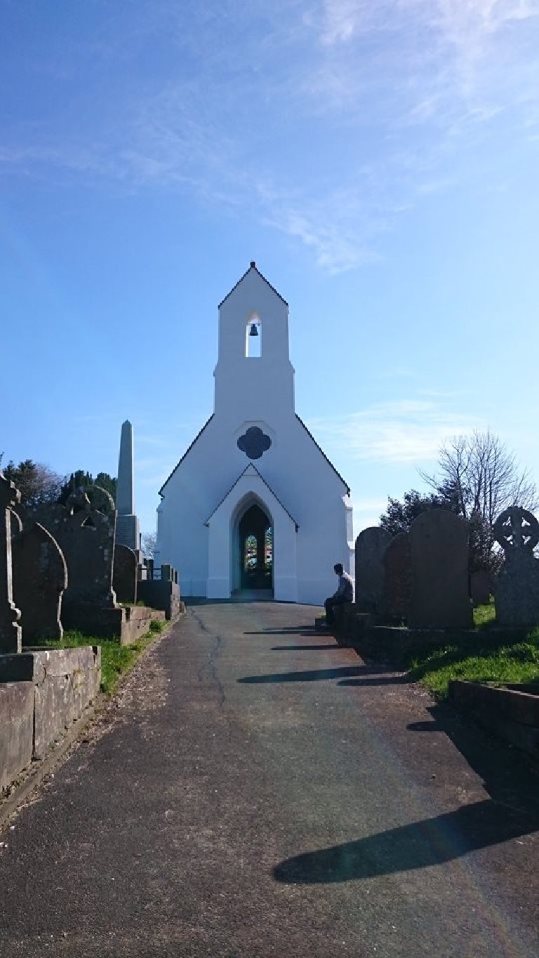 The chapel seen down the cemetery path between headstones and a stone obelisk