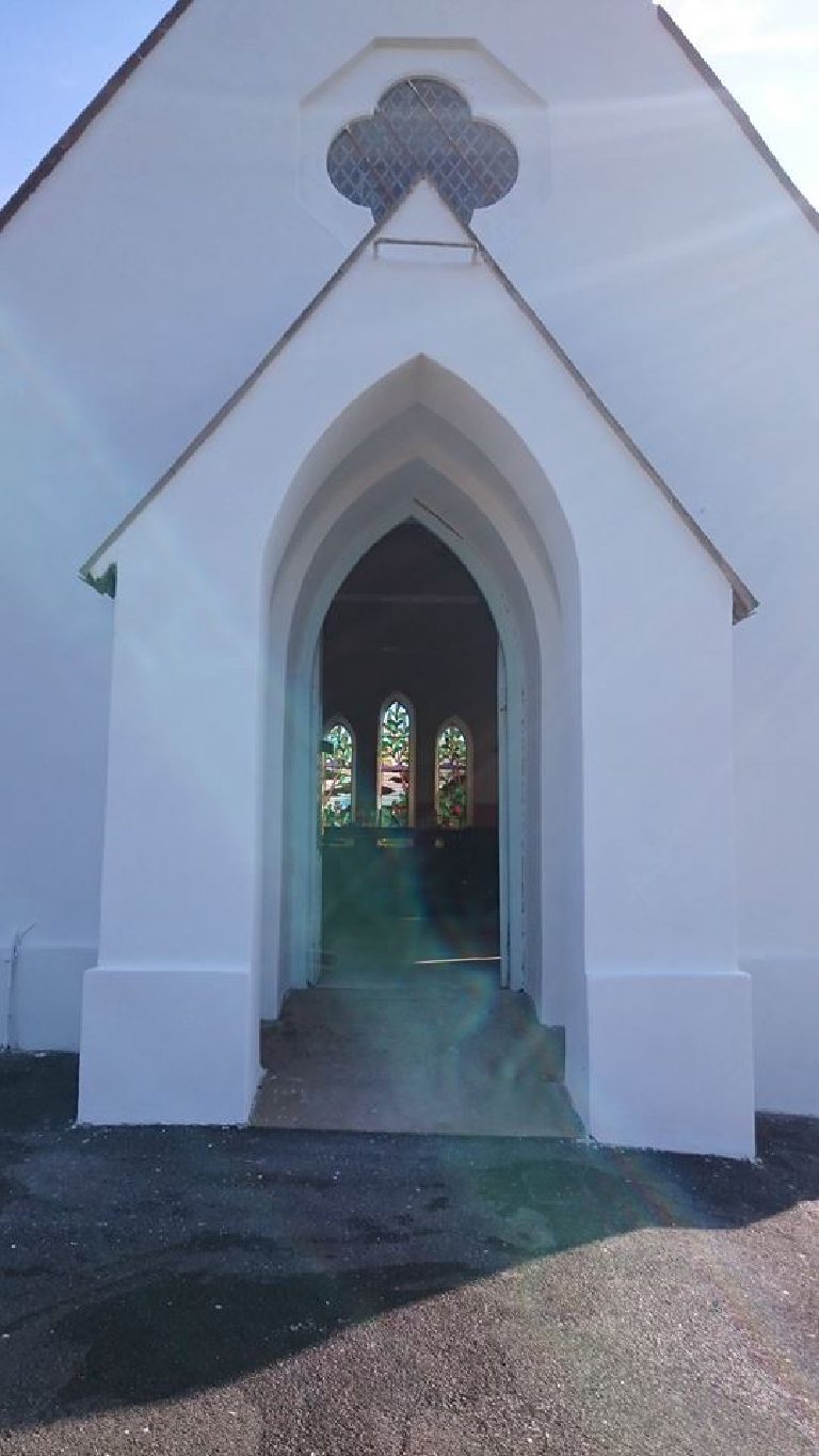 The pointed porch arch finished, stained glass visible at the far end through the open door