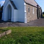 The finished chapel from the side — rendered gable, porch and bell tower, stone nave wall and slate roof