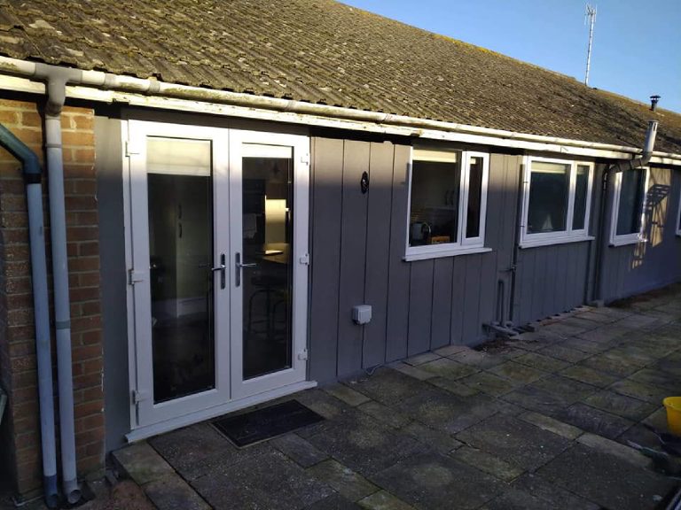 The rear elevation in low sun, with white French doors set into the grey render