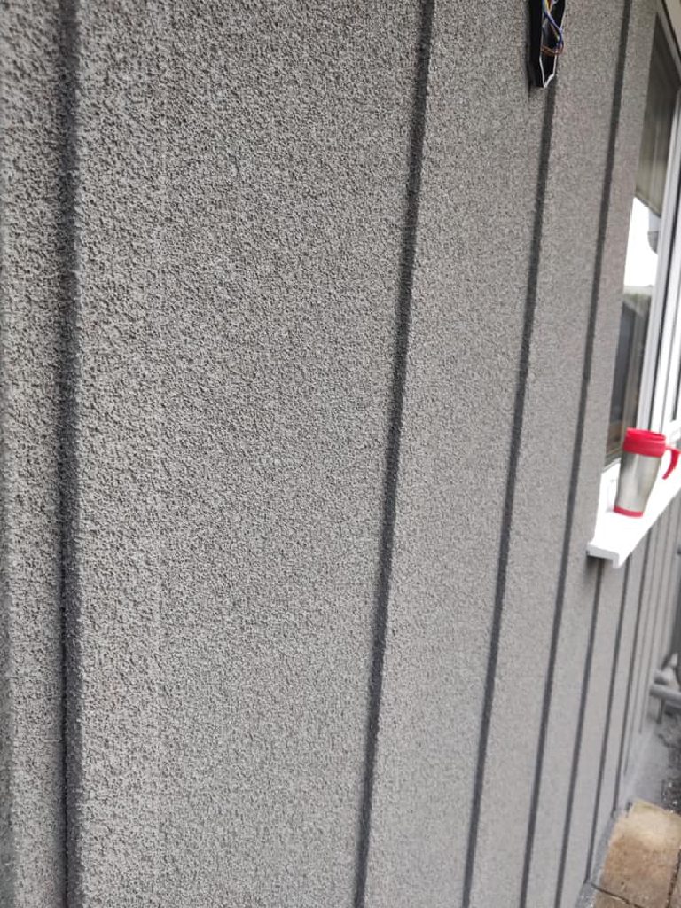 Close-up of the sprayed cork render showing its grain and the vertical cladding joints beneath