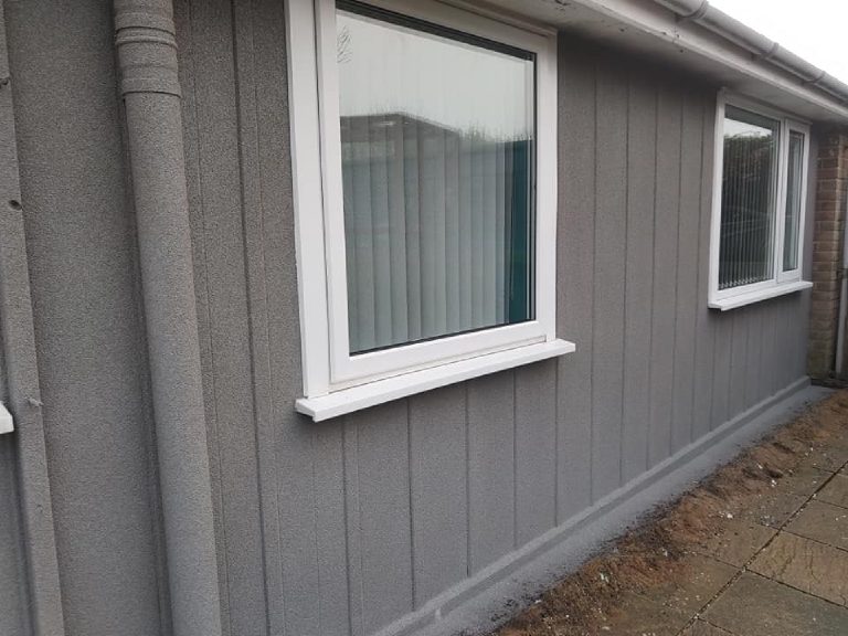 A window in the rendered wall with the render carried down to a clean plinth line at the ground