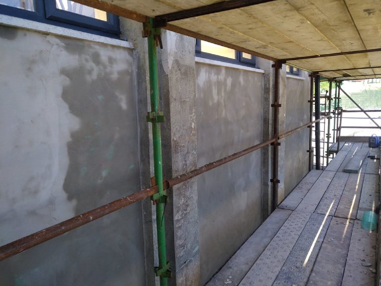 The bare, patched walls of the arcade behind the scaffold