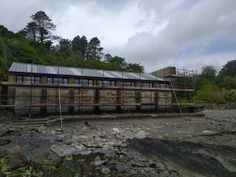 The old arcade before the work — weathered, scaffolded, standing on the shore