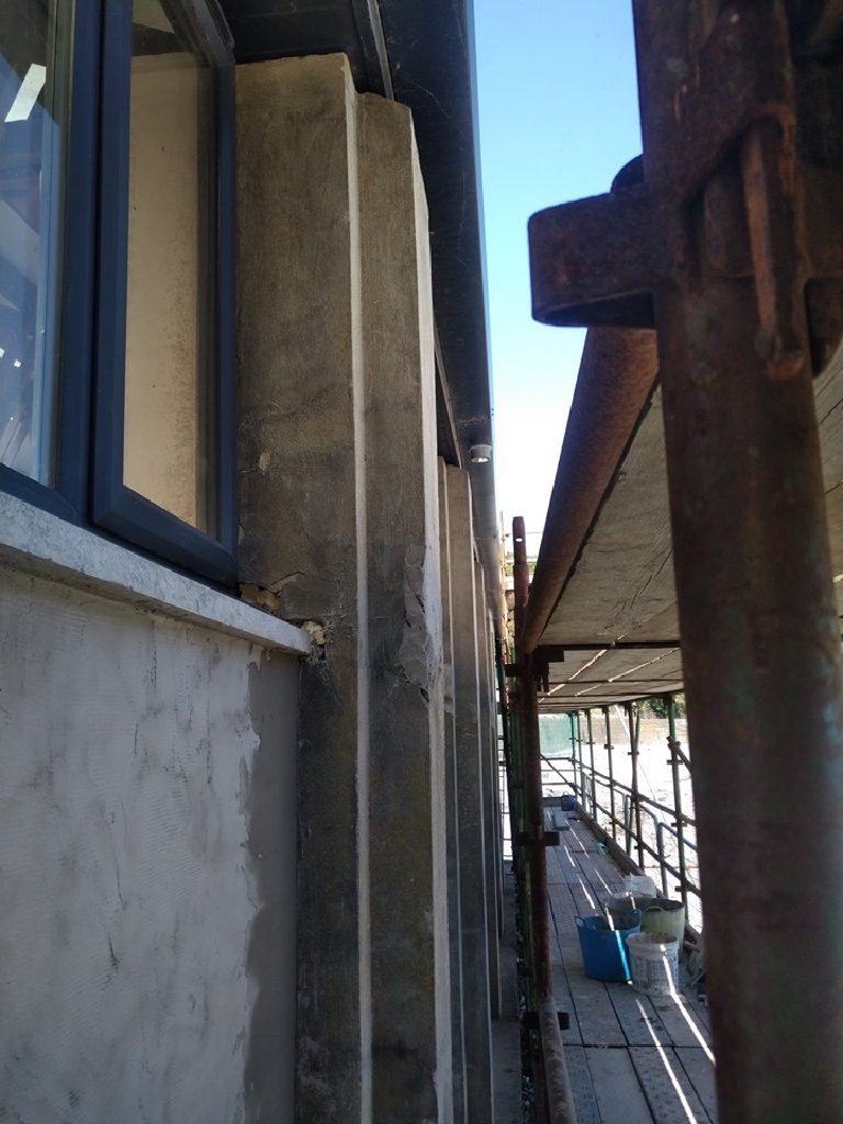 A rusted steel post at the edge of the building with the sea behind