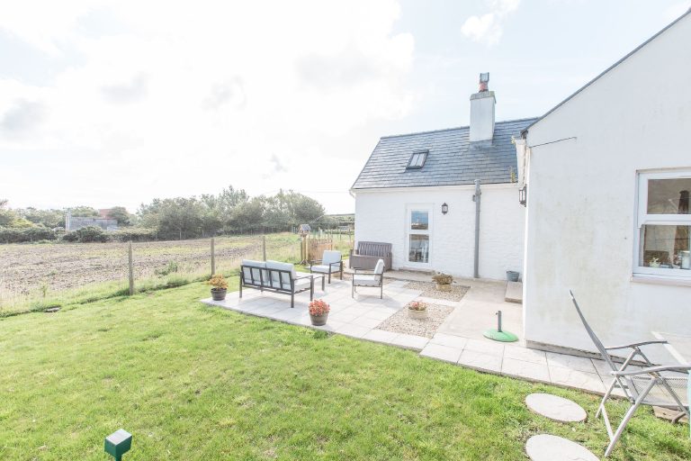 The rear of the cottage and its patio, fields running away behind