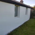 The rendered wall seen along its length, crisp window reveals and a gravel line at the base