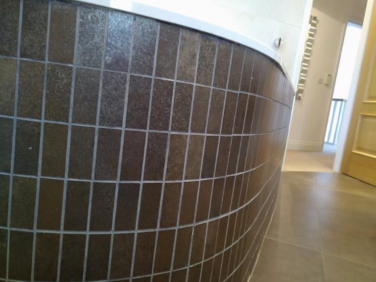 Close view of the dark mosaic tiles on the curved bath panel