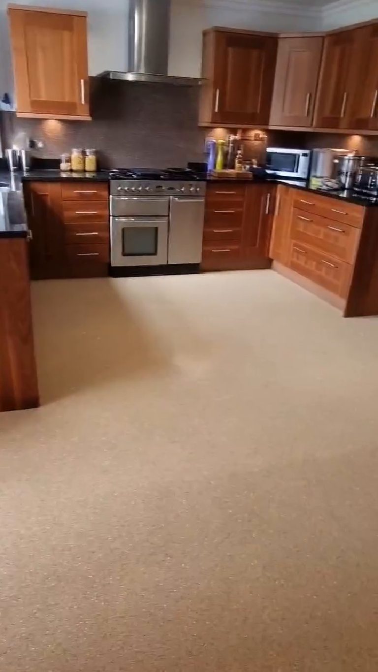 The kitchen with the sand quartz floor running wall to wall and the darker splashback behind the range