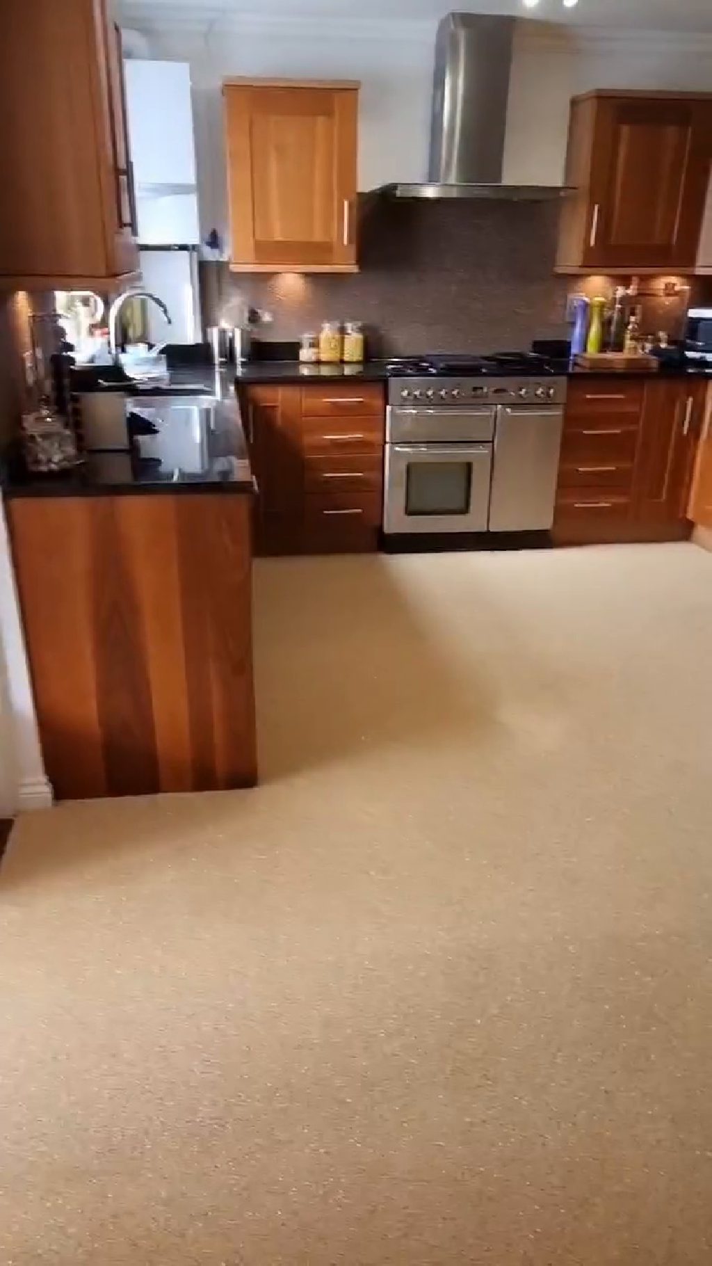 The whole kitchen from the doorway, quartz floor running wall to wall and a dark quartz splashback behind the range
