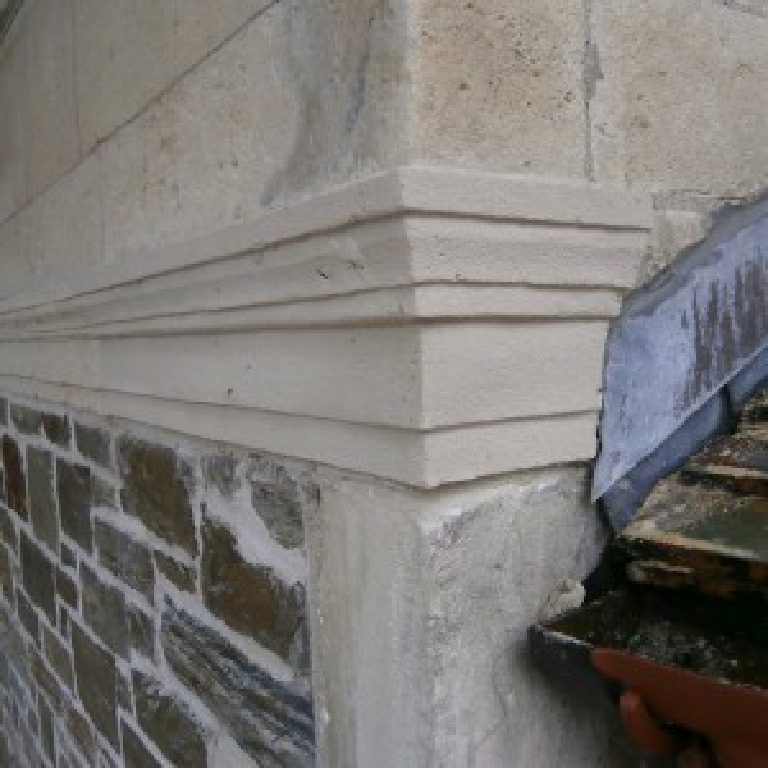 Restored corner of a moulded string course above the rubble stone wall