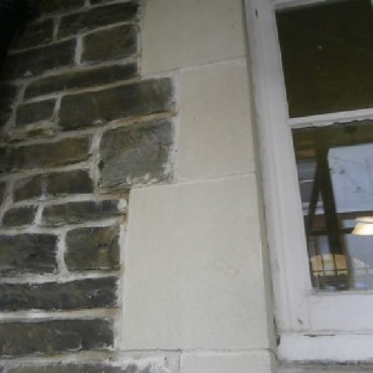 New pale jamb stones set into the dark rubble wall beside a window