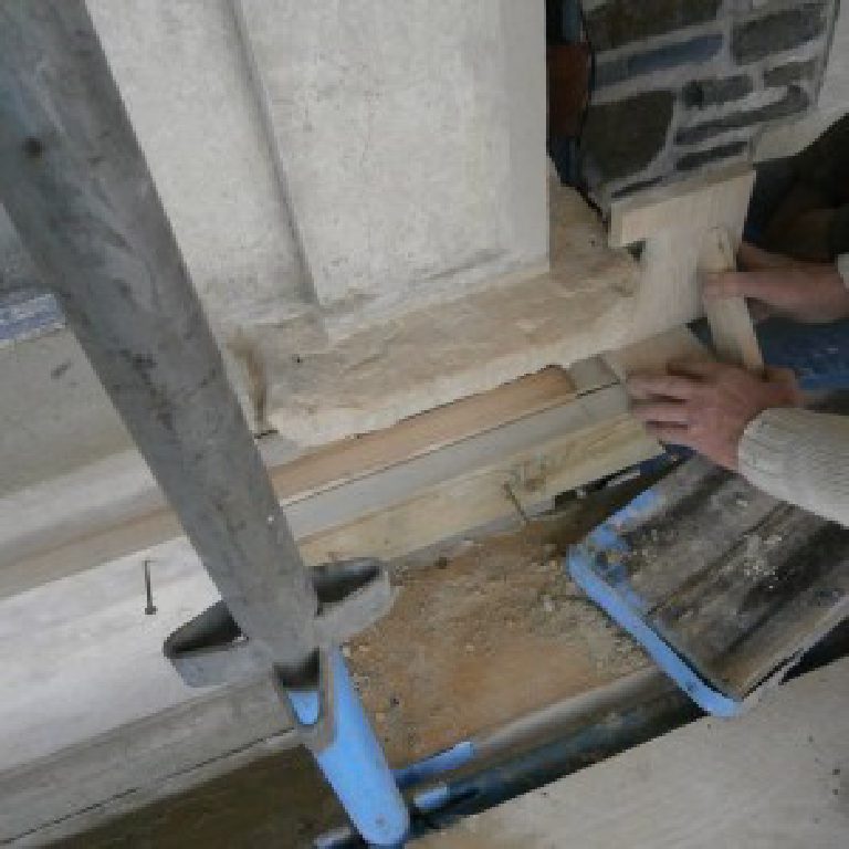 Hands at work building out a new stone sill between scaffold poles
