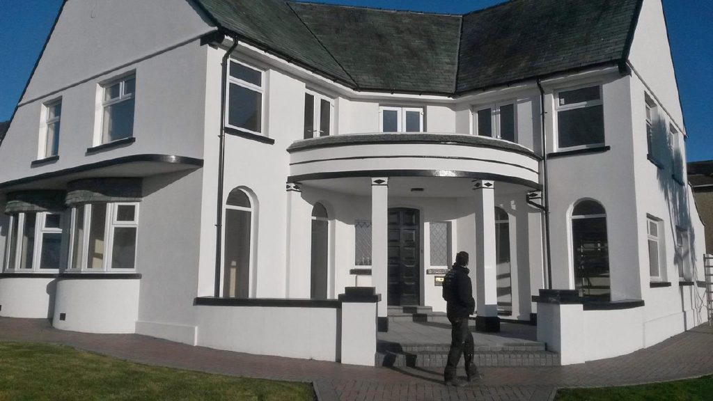 The finished house in crisp white render with black trim, plasterer at the door
