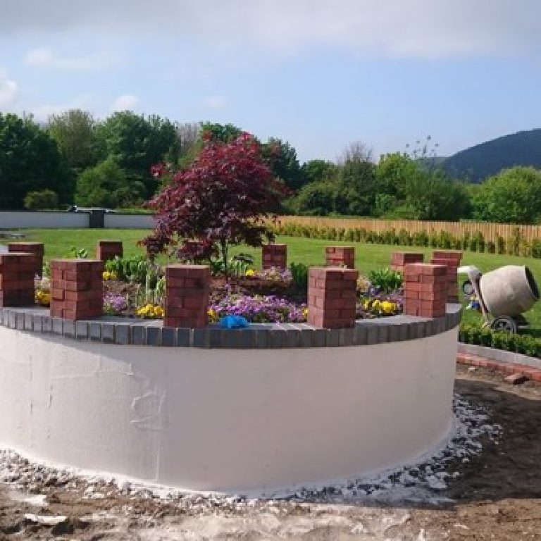 The curve freshly rendered in white, bricks stacked along the coping and a mixer standing off to the side