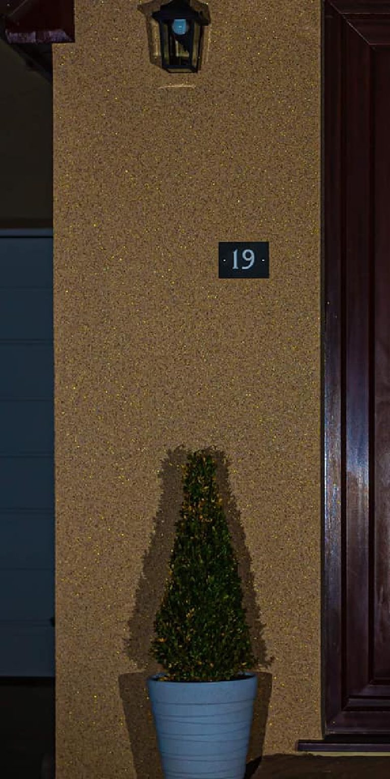 The house number and the wall beneath the lantern at night, gold flake picked out by the light