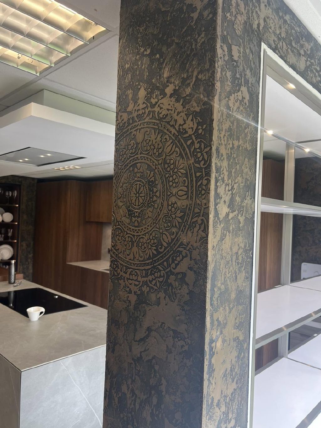 A pier in black Marmorino with a bronze finish and stencilled medallion, beside the walnut kitchen display