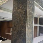 A pier in black Marmorino with a bronze finish and stencilled medallion, beside the walnut kitchen display