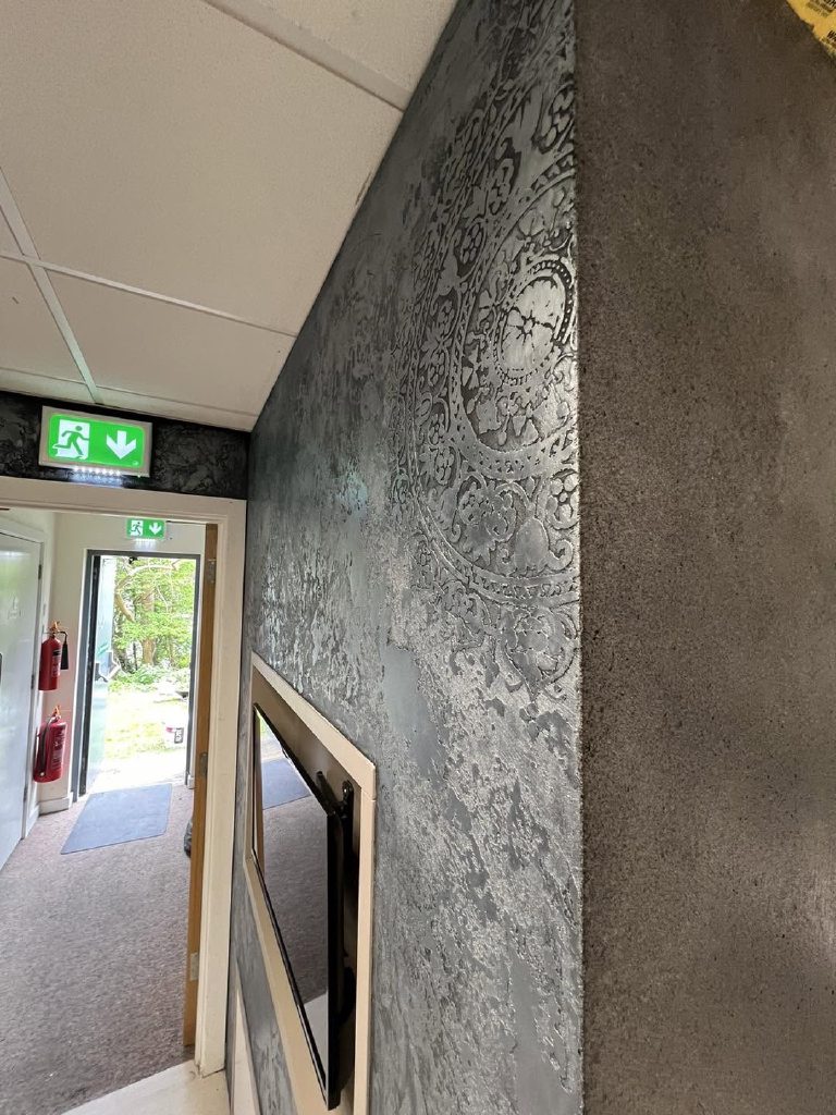 The silver-waxed wall running back to the showroom entrance, daylight raking across the stencil