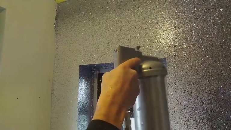 The spray gun working across a wall already covered in gun metal glitter