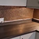 The copper and gold splashback running the length of the worktop past the ovens