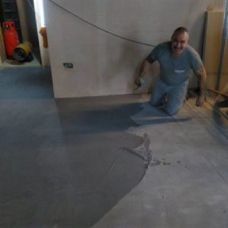 Trowelling grey MicroCement across the floor