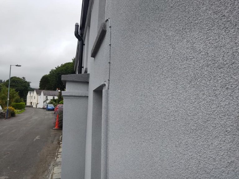 A raking view along the finished front elevation showing the render texture and the sprayed pipework