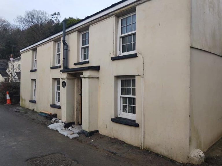 The cottage before the work — cream render, weather-streaked, with black-painted cills