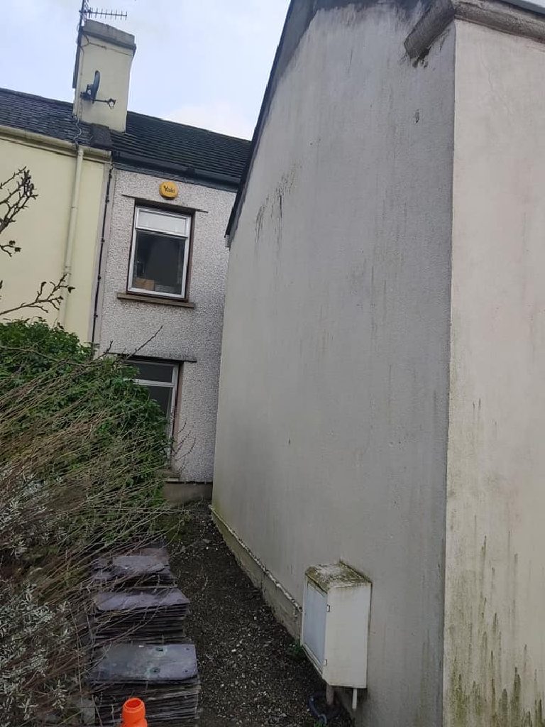 The rear gable before the work, damp-stained and streaked, with slates stacked in the passage