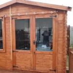 The timber garden shed from outside before the work, with festoon lights along the eaves