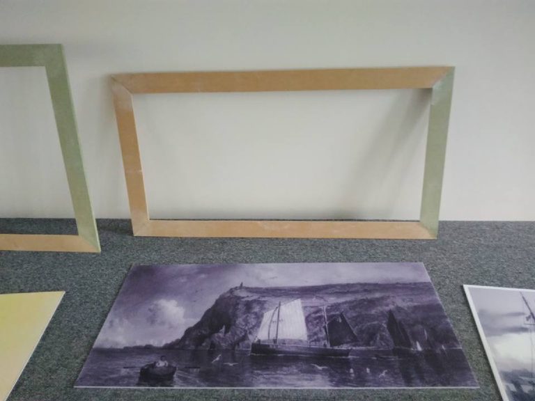 A sailing ship print laid out on the floor with frames behind