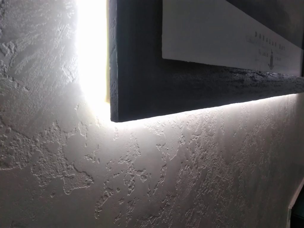 Backlighting glowing behind a MicroCement frame on the textured Marmorino wall