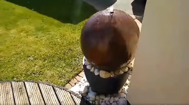 The rust sphere installed as a garden water feature beside the pond