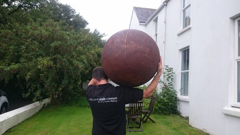 VPC plasterer carrying the rust-finished sphere on his shoulder