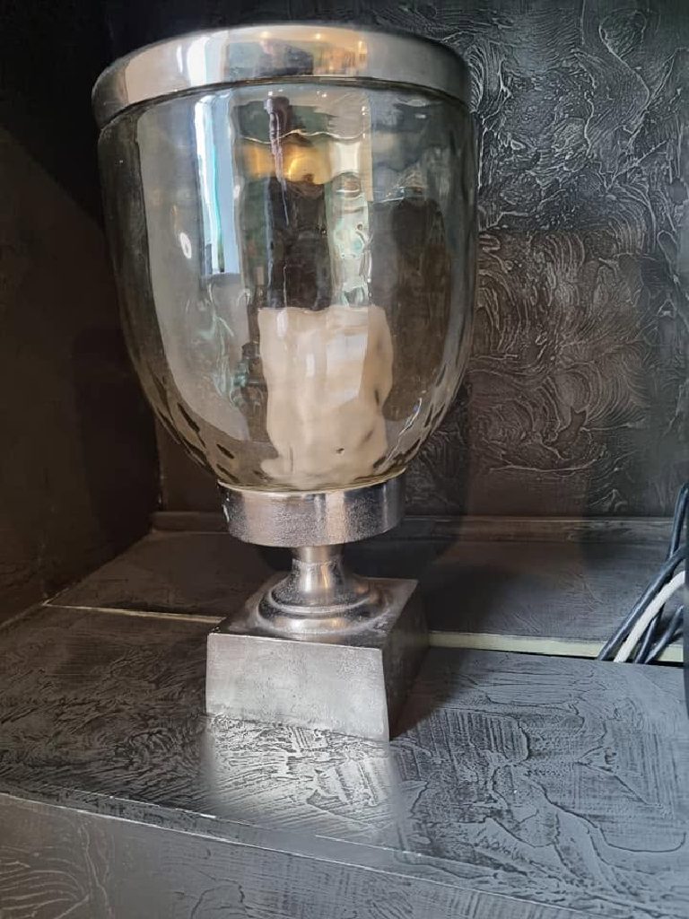 A glass and metal lamp standing on the nickel-finished shelf of a recess